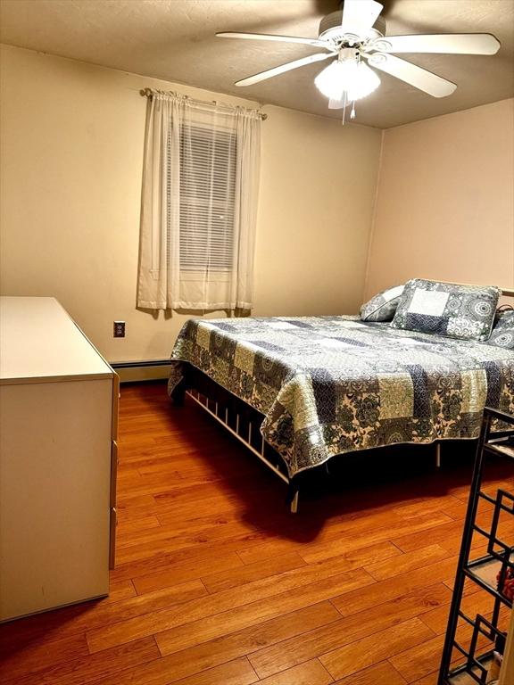 bedroom with a baseboard heating unit, wood-type flooring, and ceiling fan