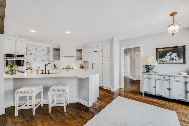 kitchen featuring open shelves, stainless steel appliances, white cabinetry, a sink, and a kitchen bar