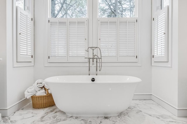 bathroom with a freestanding bath, marble finish floor, a wealth of natural light, and baseboards