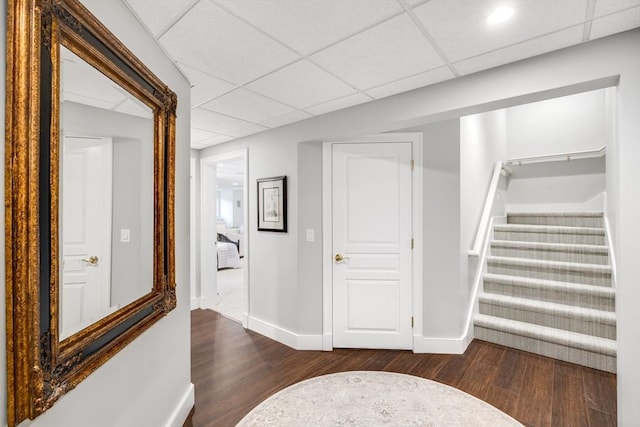 hallway featuring a paneled ceiling, dark wood-style flooring, stairway, and baseboards