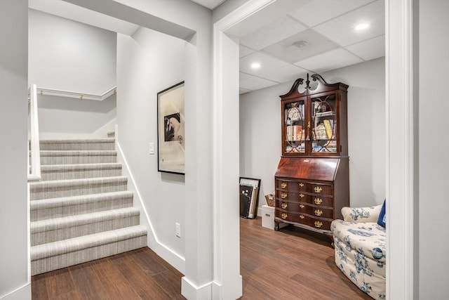 stairway featuring baseboards, a drop ceiling, wood finished floors, and recessed lighting