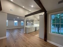 unfurnished living room featuring beam ceiling, plenty of natural light, and light hardwood / wood-style floors