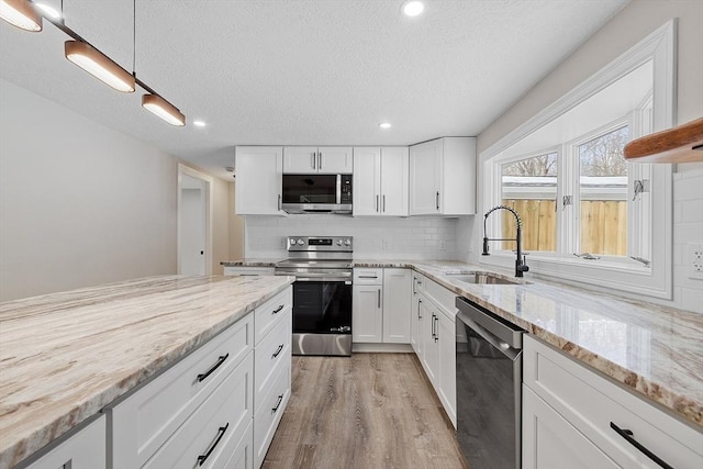 kitchen featuring a sink, white cabinets, appliances with stainless steel finishes, light wood-type flooring, and backsplash