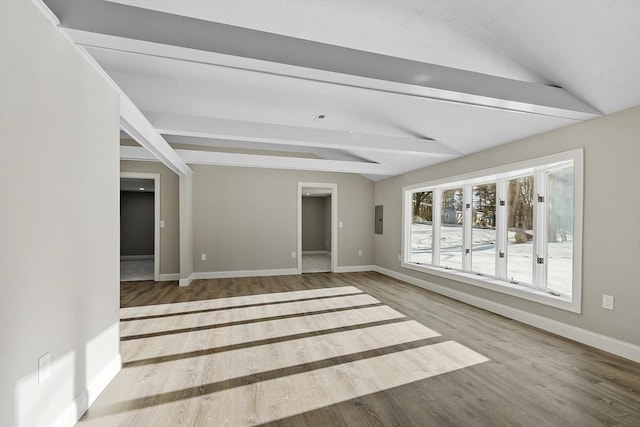 empty room featuring lofted ceiling with beams, electric panel, wood finished floors, and baseboards