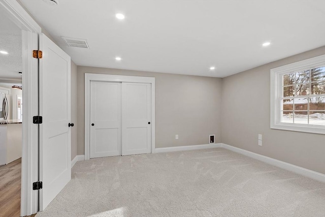 unfurnished bedroom featuring fridge, recessed lighting, light colored carpet, and visible vents