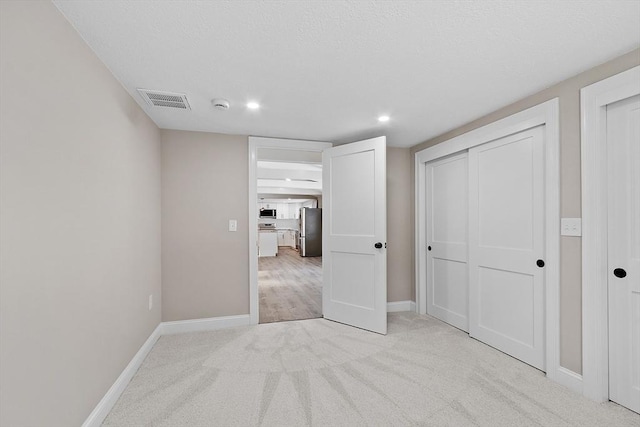 unfurnished bedroom with visible vents, light colored carpet, freestanding refrigerator, and baseboards