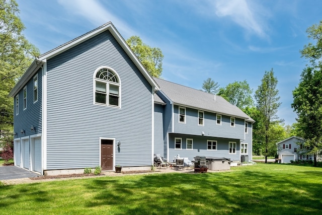 back of property featuring a lawn, a hot tub, and a garage