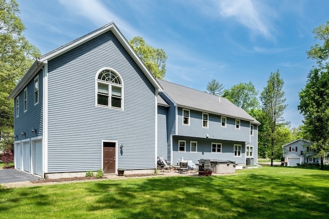 rear view of property featuring a garage, a yard, and a hot tub