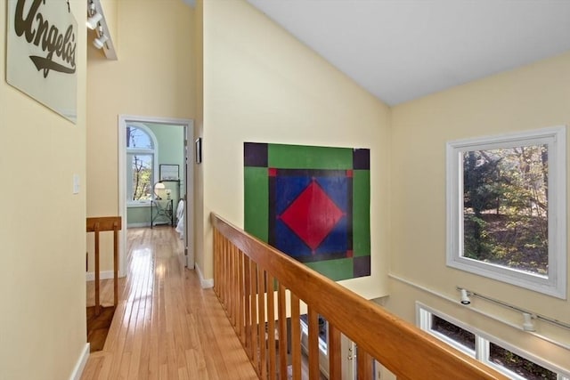 hall featuring baseboards, an upstairs landing, wood finished floors, and lofted ceiling
