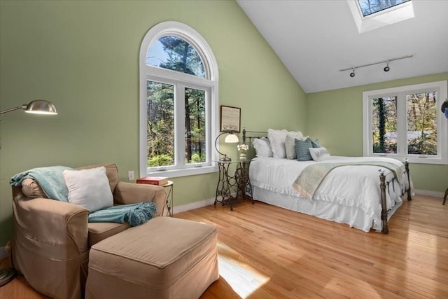 bedroom featuring track lighting, baseboards, high vaulted ceiling, light wood-style flooring, and a skylight