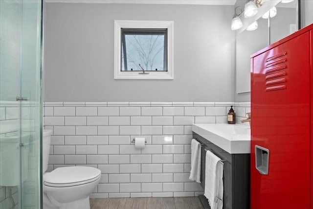 bathroom featuring tile walls, a shower stall, a wainscoted wall, vanity, and toilet