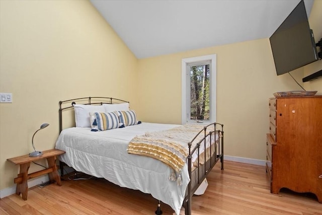 bedroom featuring baseboards, vaulted ceiling, and light wood-style flooring
