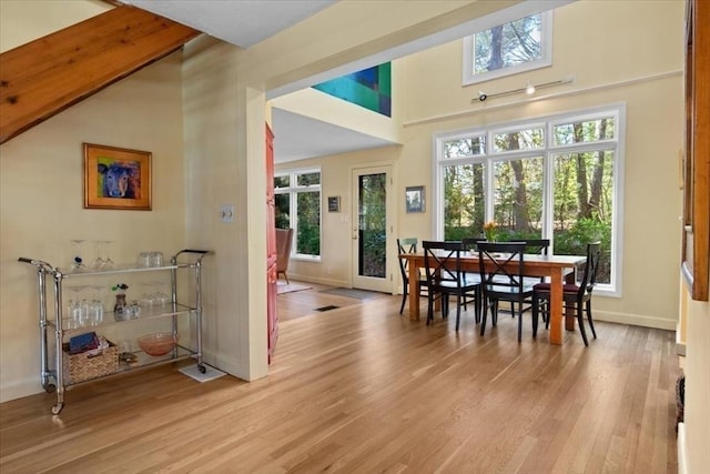 dining area featuring light wood-style floors, baseboards, and a towering ceiling