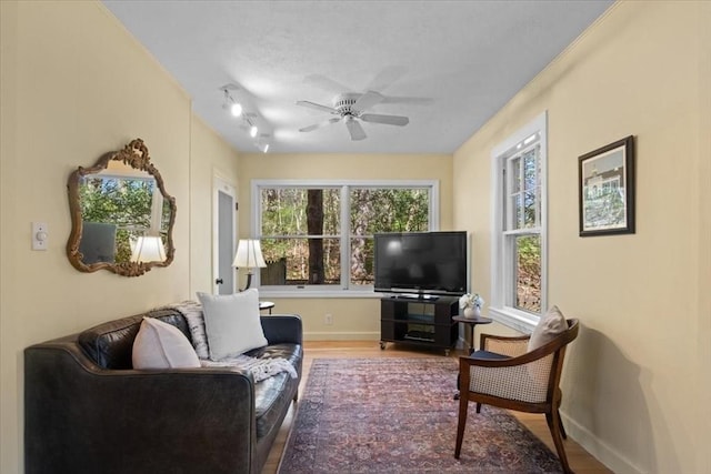 living room featuring baseboards, a ceiling fan, a textured ceiling, and wood finished floors