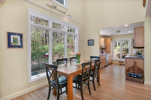 dining area featuring light wood-style floors, baseboards, and a towering ceiling