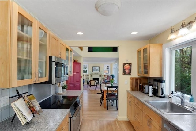 kitchen featuring glass insert cabinets, electric range oven, a sink, stainless steel microwave, and light wood-style floors