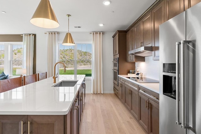 320 Martins Lndg Unit 307, North Reading, MA 01864 - kitchen featuring appliances with stainless steel finishes, a sink, under cabinet range hood, light wood-style floors, and an island with sink