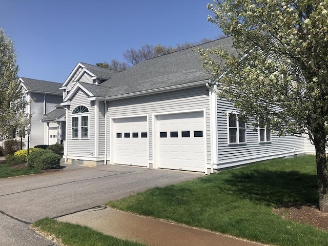 view of front of house featuring roof with shingles, an attached garage, driveway, and a front yard