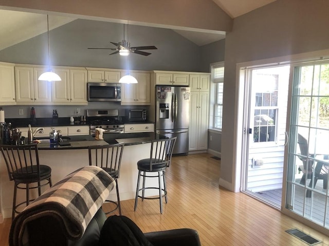 kitchen with stainless steel appliances, dark countertops, vaulted ceiling, and a breakfast bar