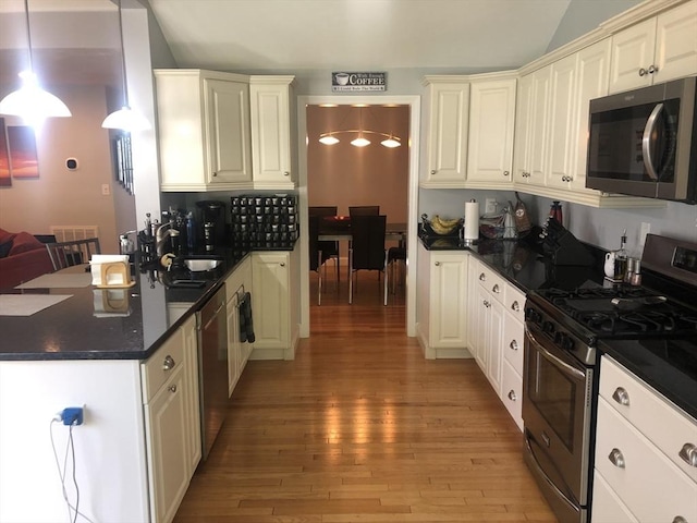 kitchen featuring light wood-type flooring, a peninsula, dark countertops, and stainless steel appliances