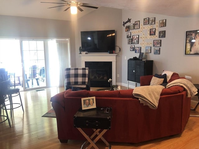 living room with wood finished floors, a ceiling fan, a glass covered fireplace, and lofted ceiling