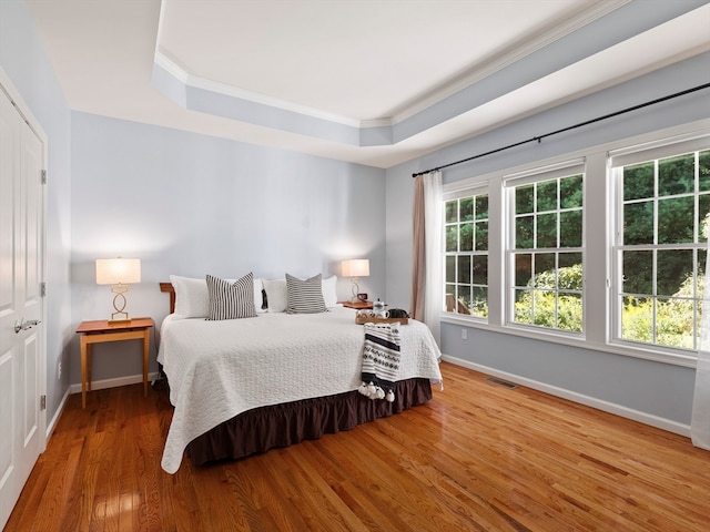 bedroom with a tray ceiling, ornamental molding, and hardwood / wood-style flooring