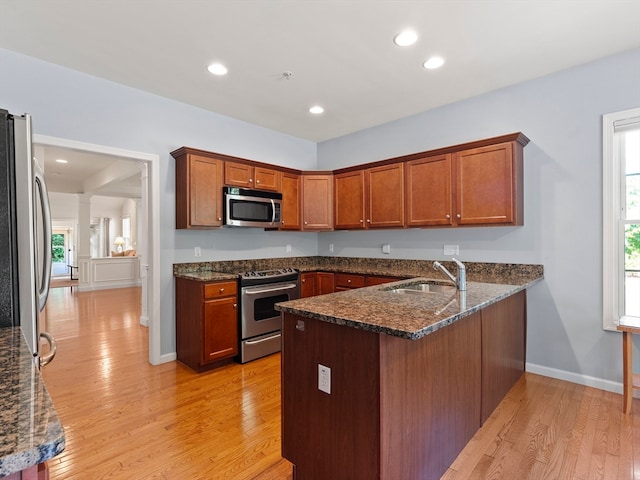 kitchen featuring appliances with stainless steel finishes, dark stone countertops, light hardwood / wood-style floors, and kitchen peninsula