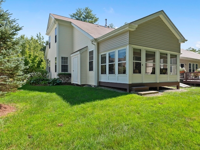 back of property with a sunroom, a deck, and a lawn