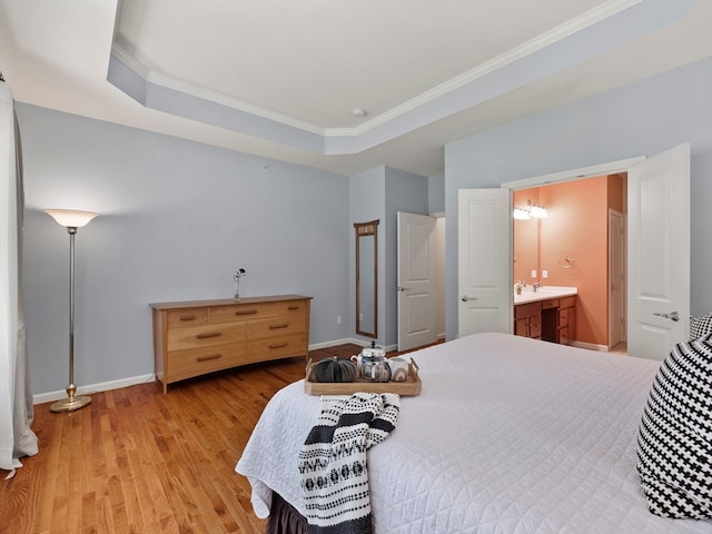 bedroom featuring a raised ceiling, light hardwood / wood-style floors, crown molding, and ensuite bath