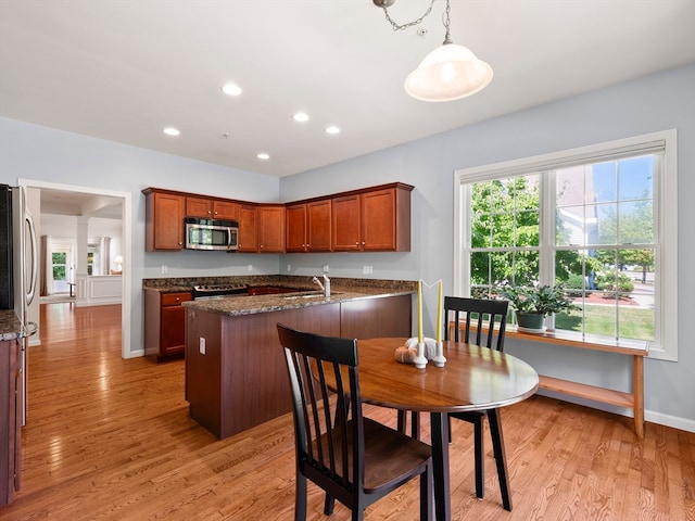 kitchen featuring pendant lighting, stainless steel appliances, dark stone counters, and light hardwood / wood-style floors