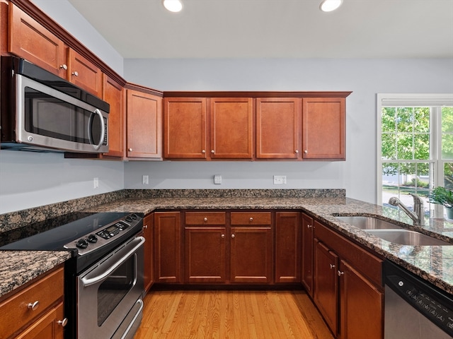 kitchen featuring light hardwood / wood-style flooring, stainless steel appliances, sink, and dark stone countertops