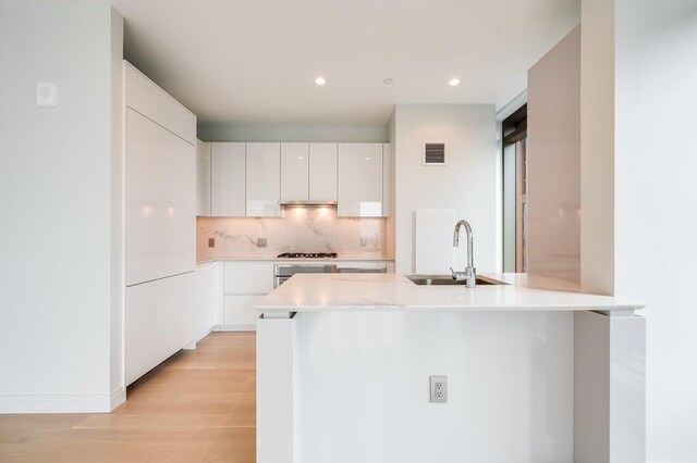 kitchen featuring white cabinetry, sink, stainless steel gas cooktop, decorative backsplash, and light wood-type flooring