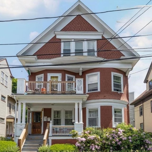 victorian house featuring a balcony, covered porch, and a shingled roof