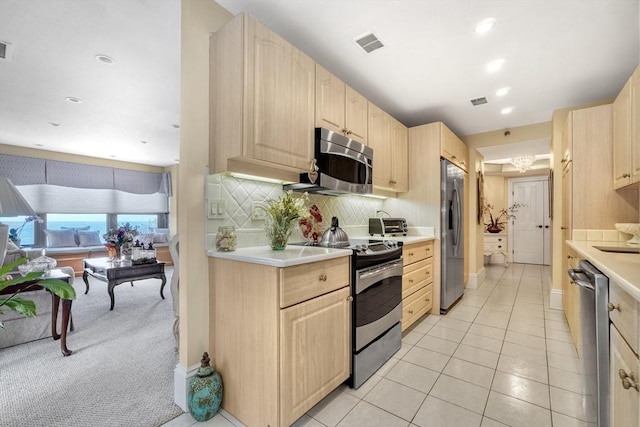 kitchen with appliances with stainless steel finishes, backsplash, light tile patterned floors, and light brown cabinetry