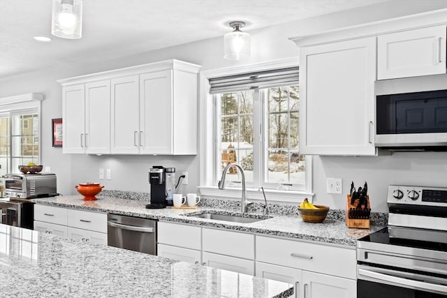 kitchen featuring stainless steel appliances, white cabinetry, sink, and decorative light fixtures