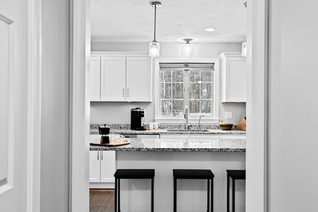 kitchen with sink, a breakfast bar area, light stone counters, white cabinets, and decorative light fixtures