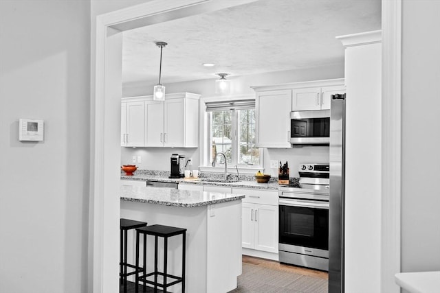 kitchen featuring appliances with stainless steel finishes, a breakfast bar, sink, white cabinets, and hanging light fixtures