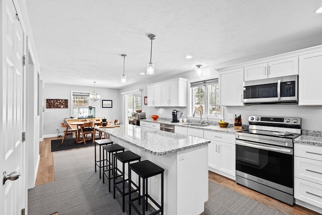 kitchen featuring white cabinetry, appliances with stainless steel finishes, hanging light fixtures, and a kitchen island