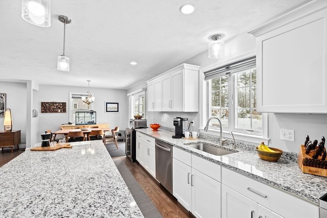 kitchen featuring sink, light stone counters, hanging light fixtures, stainless steel dishwasher, and white cabinets