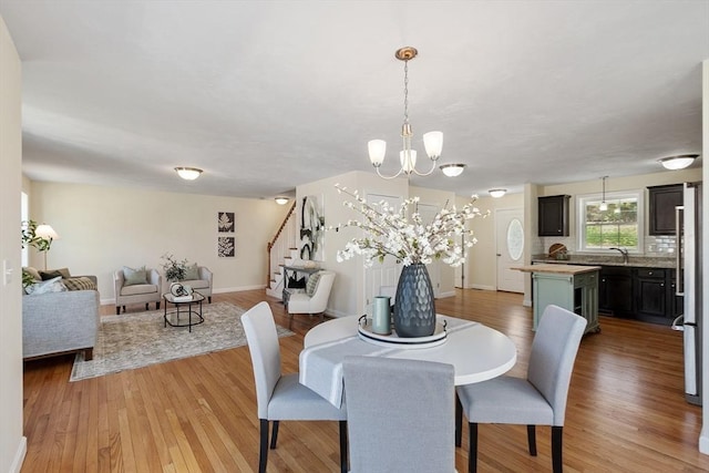 dining area with baseboards, a notable chandelier, stairs, and light wood-type flooring