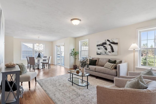 living room with a notable chandelier, light wood-type flooring, and a healthy amount of sunlight