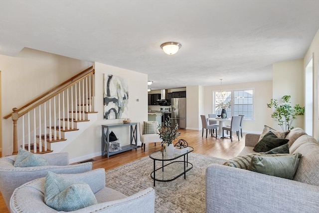 living area featuring a chandelier, light wood-style floors, baseboards, and stairs