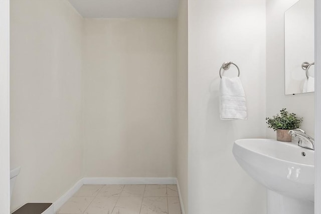 half bathroom featuring marble finish floor, baseboards, toilet, and a sink