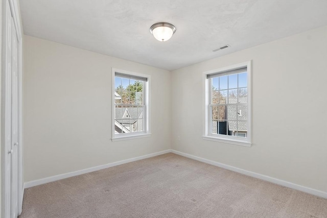carpeted spare room with a wealth of natural light, visible vents, and baseboards
