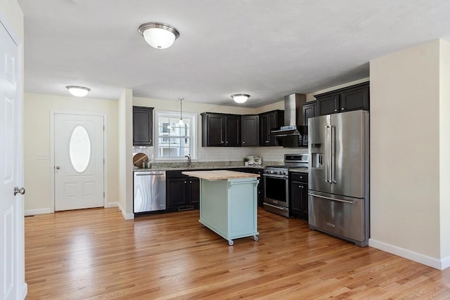 kitchen with light wood finished floors, stainless steel appliances, light countertops, wall chimney range hood, and a kitchen island