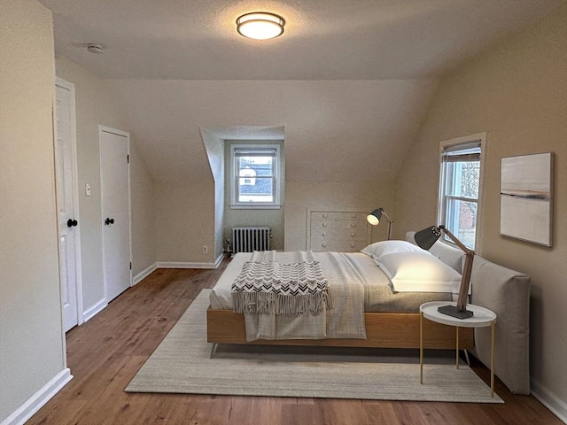 bedroom with radiator heating unit, hardwood / wood-style floors, a textured ceiling, and vaulted ceiling