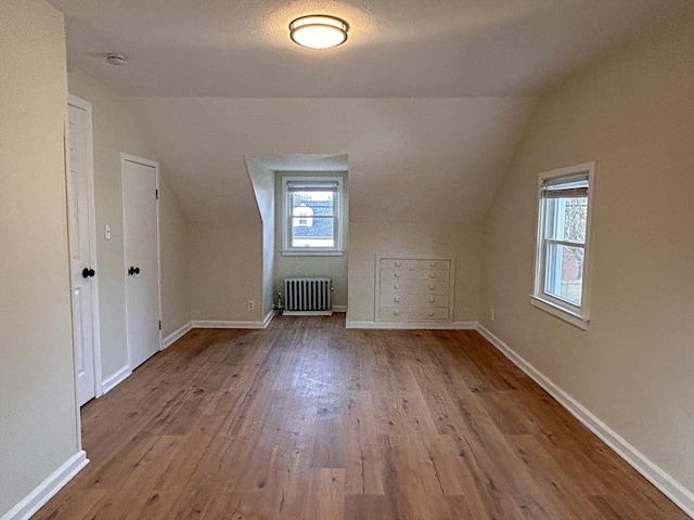 additional living space with light wood-type flooring, radiator heating unit, a textured ceiling, and lofted ceiling