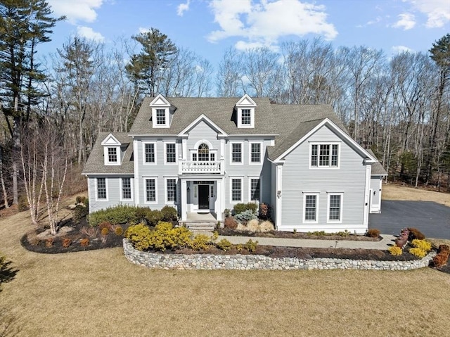 view of front of home with a front yard, a balcony, and a shingled roof