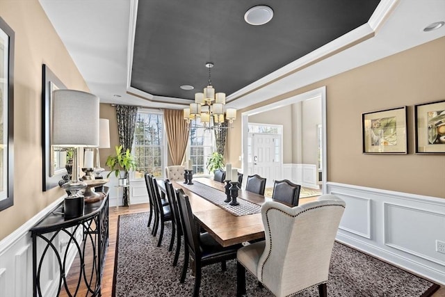 dining room with a chandelier, a wainscoted wall, wood finished floors, a decorative wall, and a raised ceiling