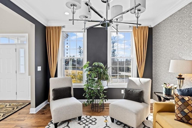 living area with wood finished floors, wallpapered walls, an accent wall, and ornamental molding